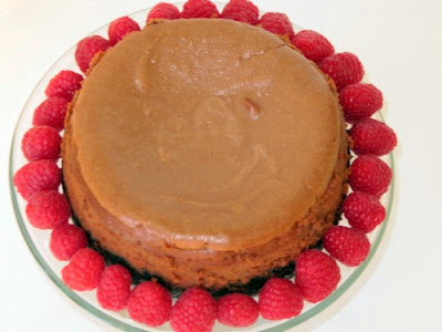 Top view image of a whole round rich double chocolate cheesecake ringed with fresh raspberries on a glass cake stand.