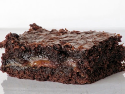 closeup of one fudgy chocolate caramel  brownie sitting on a piece of white parchment paper.