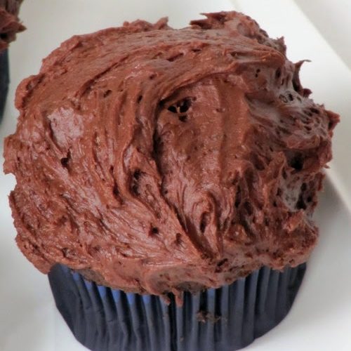 closeup top view of a chocolate cupcake frosted with a layer of thick creamy chocolate buttercream .