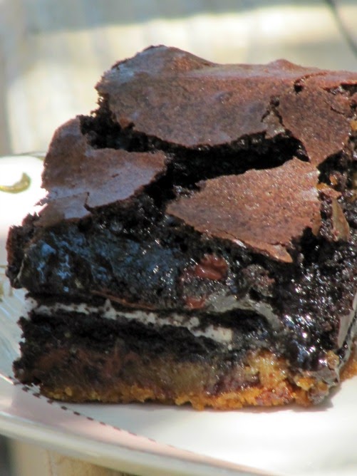 closeup of gooey chocolate slutty brownies with a crinkled flaky topping an oreo cookie center and chocolate chip cookie base on a white plate.