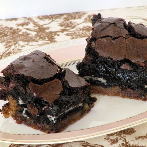 a white plate holds two rich fudgy slutty brownies with gooey Oreo centers and a chocolate chip cookie base