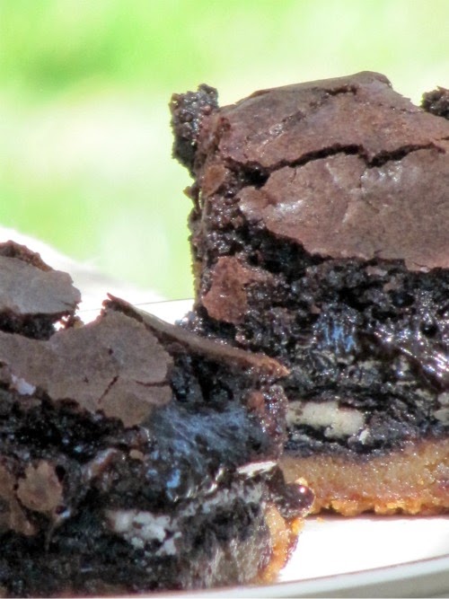 Two fudge slutty brownie squares consisting of a crisp chocolate chip cookie base, Oreo stuffed centers and a top layer of fudge brownie mix are sitting on a white plate