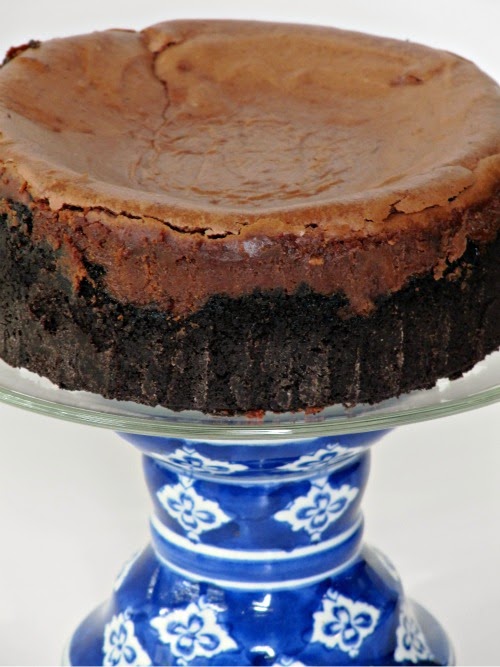 whole triple chocolate cheesecake on a cake stand with a blue and white base.