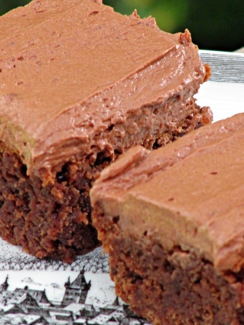 two rich Joy the Baker Chocolate Frosted Brownies on a piece of white parchment paper.