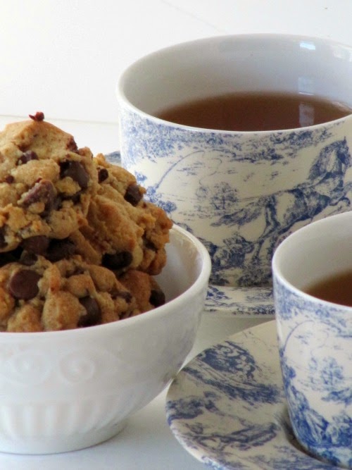 White bowl of browned butter chocolate chip cookies next to two blue and white cups and saucers filled with coffee. 