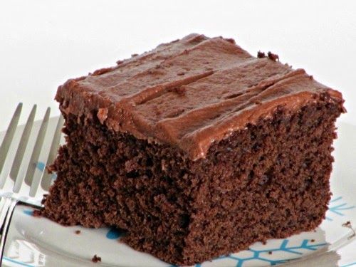 Close up of a square piece of dark chocolate cocoa buttermilk cake with cocoa mascarpone frosting on a white plate.
