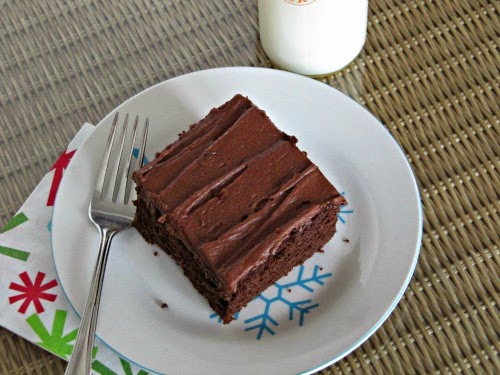 Top view of a square piece of dark chocolate buttermilk sheet ake with cocoa mascarpone frosting on a white plate next to a glass bottle of milk.