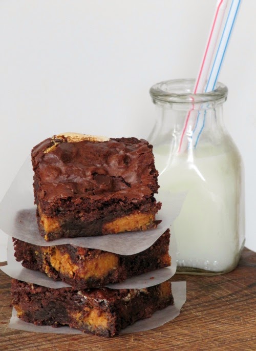 a closeup front view of a large glass bottle of milk next to a stack of three fluffernutter brownies made with brownie mix, reese's peanut butter eggs, mini-marshmallows and chocolate chips.