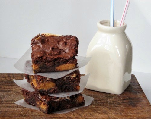 A stack of fluffernutter brownies filled with reese's peanut butter candies sitting on a brown wood table top next to a bottle of milk.