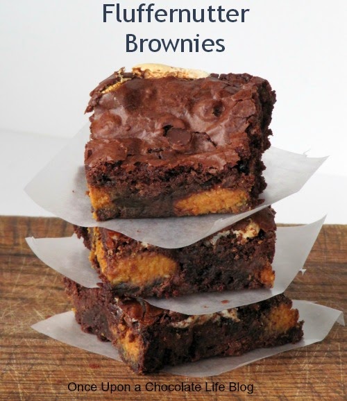 Stack of three fluffernutter brownies made with peanut butter candy eggs with marshmallows and chocolate chip filling sitting on a brown table top with white parchment squares separating each brownie.