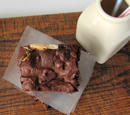 overhead view of a single fluffernutter brownie made with Reese's peanutbutter eggsresting on a piece of parchment paper next to a bottle of milk on a brown table.