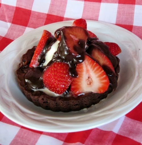 Fresh Fruit Brownie Tart Sundae covered with vanilla ice cream, chocolate fudge sauce and sliced strawberries on a white plate.