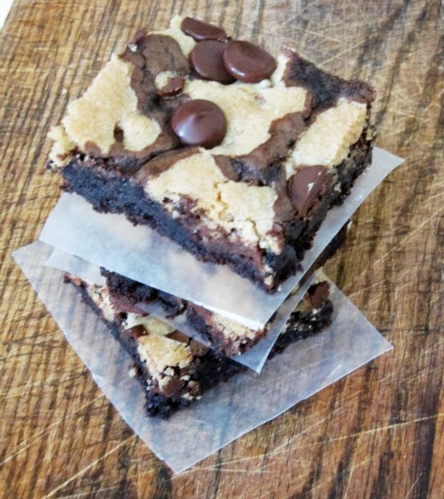 Overhead view of two rich fudgy chocolate chip cookie brownies separated by a piece of parchment paper sitting on a brown table top.