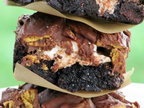 Closeup side view of a stack of chocolate s'mores brownies with a fudgy brownie base, melted marshmallow center and chocolate and graham cracker topping. 