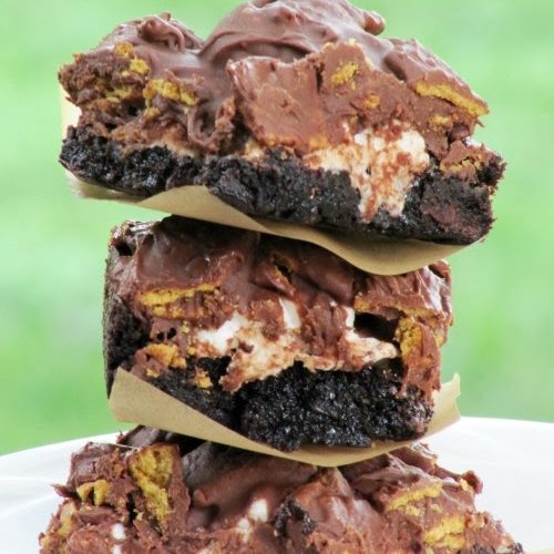 Stack of three rich gooey s'more brownies separated with white parchment paper. Brownies are made with brownie mix, mini marshmallows, graham cracker cereal and melted chocolate chips