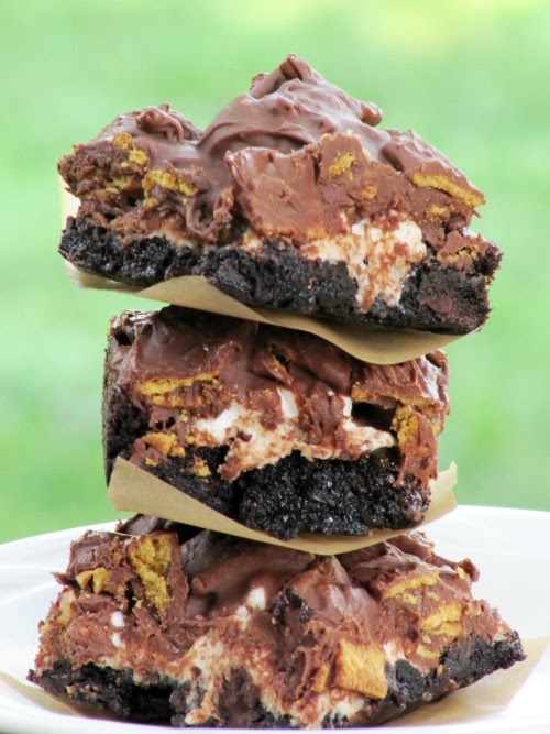 Stack of three rich gooey s'more brownies separated with white parchment paper. Brownies are made with brownie mix, mini marshmallows, graham cracker cereal and melted chocolate chips