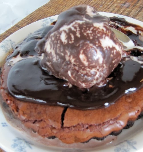 Fudge brownie tart From Southern Living Magazine in a tart pan wtih hot fudge and vanilla ice cream topping on a serving platter set on a cutting board.