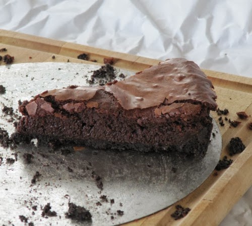 side view of a slice of rich fudge brownie tart from Southern Living Magazine surrounded by crumbs on a white serving platter.