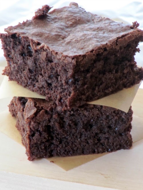 A closeup image of two stacked Guittard truffle brownies with brown parchment paper inbetween them. 