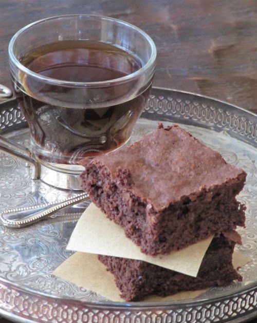 a glass cup of coffee is sitting on a table behind a stack of two rich Guittard truffle brownies.