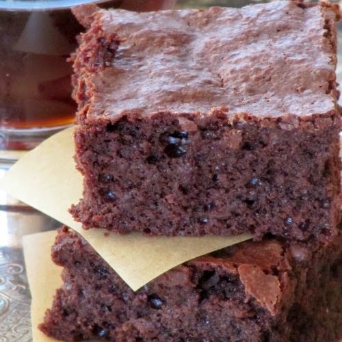 a closeup of a stack of two fudgy guittard chocolate truffle brownies separated by a piece of white parchment paper. THe brownies are on a surface in front of a cup of coffee