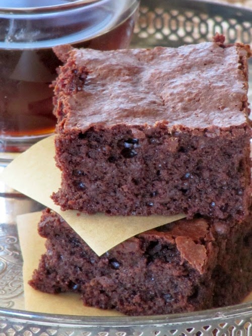 a closeup of a stack of two fudgy guittard chocolate truffle brownies separated by a piece of white parchment paper. THe brownies are on a surface in front of a cup of coffee