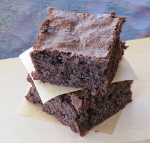 Two fudgy guittard truffle brownies are stacked with parchment paper in between are sitting on a light tan surface.