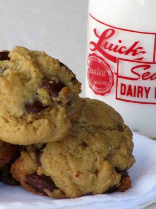 Soft Ritz Carlton chocolate chip cookies on a white plate next to a glass milk bottle.