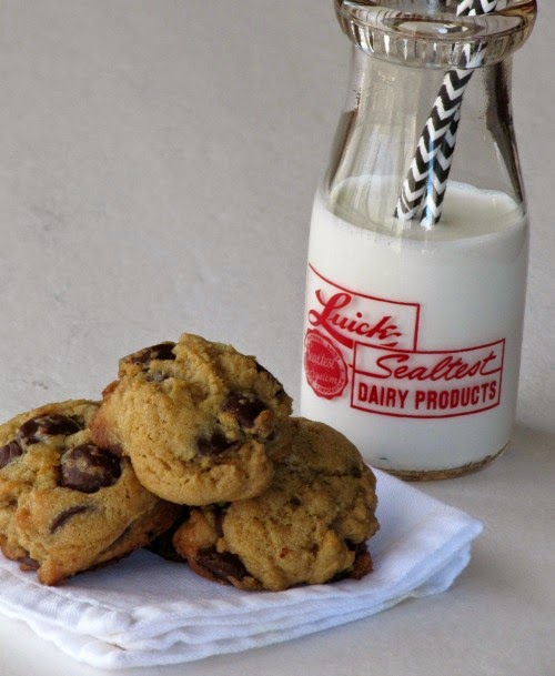 Soft chocolate chip cookies on a white plate next to a glass jar of milk.
