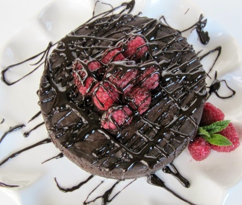 Top view of round decadent chocolate cake with chocolate glaze dripping on it garnished with fresh strawberries in the center on a white platter