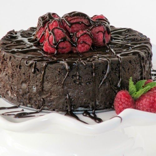 close-up of a Top view of round decadent chocolate cake with chocolate glaze dripping on it garnished with a mound of fresh strawberries in the center on a white platter