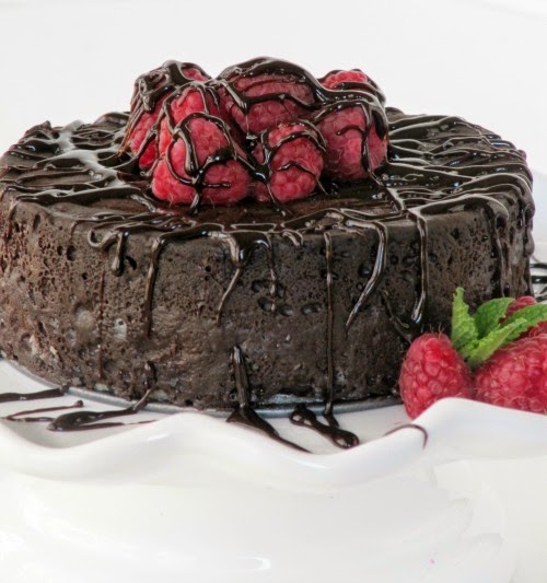 close-up of a Top view of round decadent chocolate cake with chocolate glaze dripping on it garnished with a mound of fresh strawberries in the center on a white platter