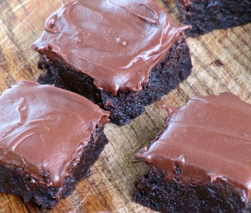 closeup of fudgy dark double  chocolate bourbon brownies with hershey's chocolate frosting on a brown wood surface.