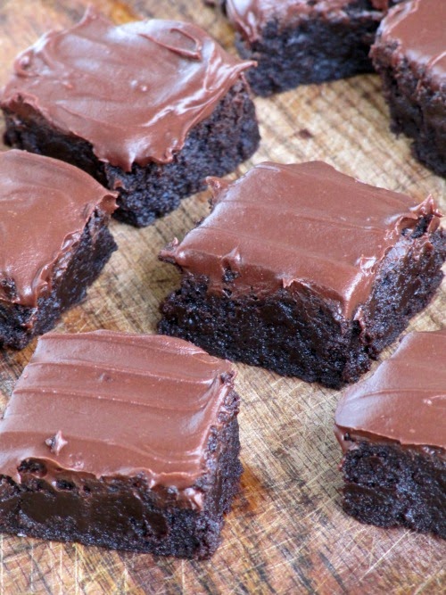closeup view of rich double chocolate bourbon brownies with   Hershey's chocolate frosting. The brownies are are sitting on a dark brown wood surface.