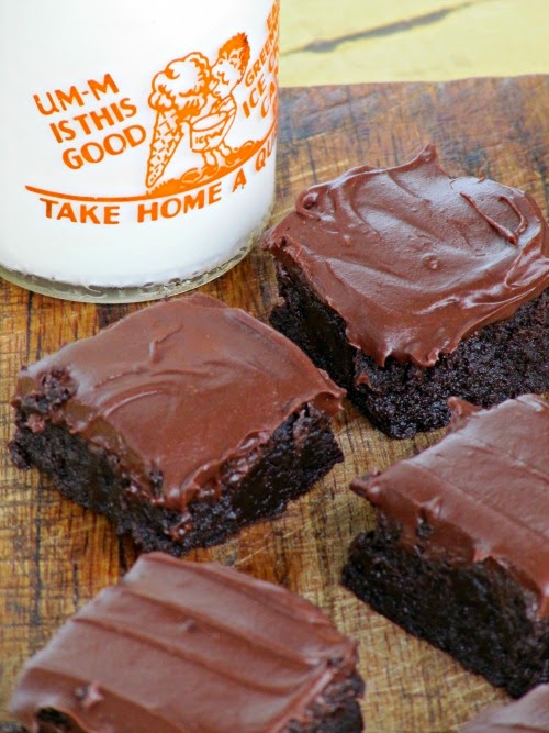 overhead view of four double chocolate bourbon brownies with Hershey's chocolate frosting in front of a glass bottle of milk.