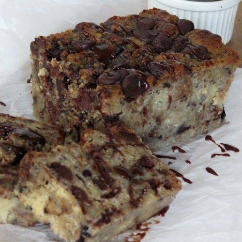 Two slices of Bailey's chocolate chip cookie bread pudding on a white platter with chocolate fudge sauce in a white cup