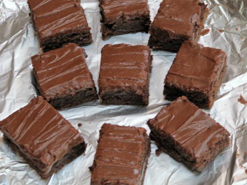 Nine fudgy chocolate frosted lunch lady brownies scattered on a piece of white parchment paper.