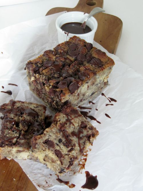 Three large pieces of Southern-style chocolate chip cookie bread pudding on white parchment with a small white cup of chocolate fudge sauce.