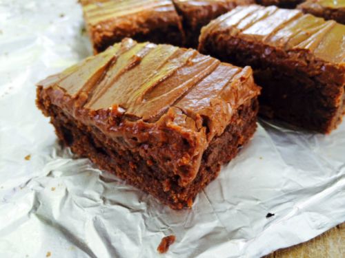 close up image of three rich chocolate lunch lady brownies with thick fudge frosting on a piece of crumpled white parchment paper.