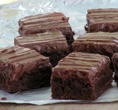 Several thick chocolate lunch lady brownies with chocolate frosting sitting on a piece of white parchment paper