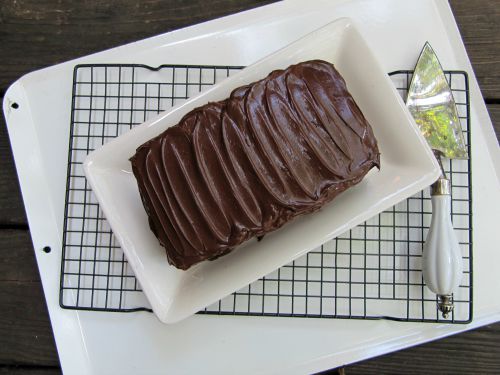 top view of rectangular Beatty's chocolate cake frosted with dark chocolate buttercream icing on a white platter sitting on a wire rack.