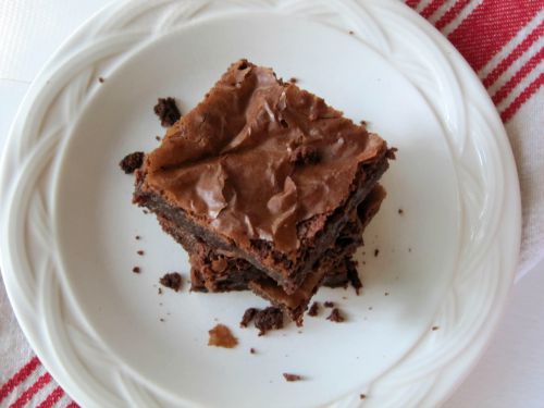 top view of a single deliciously fudgy chocolate Connie's PMS brownie on a white plate with crumbs around it.