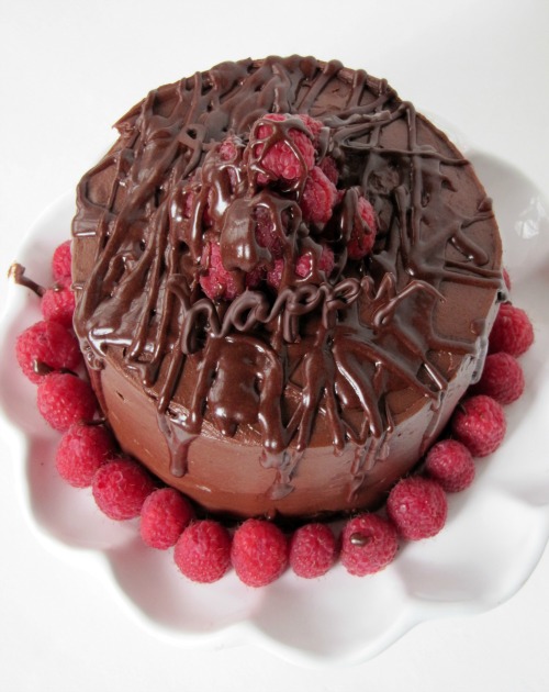Top view of a rich chocolate frosted chocolate buttermilk  cake covered in whipped buttercream chocolate frosting with a pile of fresh raspberries garnishing the top and a chocolate drizzle all over and a ring of fresh raspberries around the base of the cake.