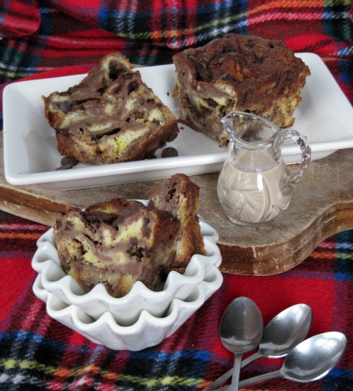 Three servings of creamy Bailey's chocolate brioche bread pudding with melted dark chocolate chunks and Bailey's Irish Cream flavoring on white serving dishes and bowls.