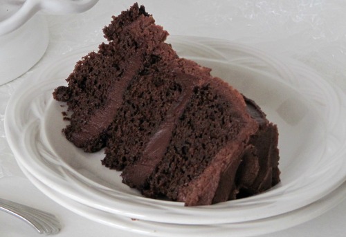 slice of three-layer dark chocolate blackout cake on a stack of white plates