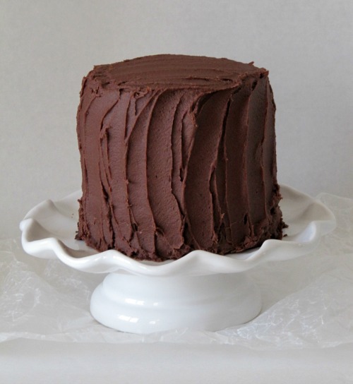 Three layer iced dark chocolate cake with chocolate frosting on a white cake stand.