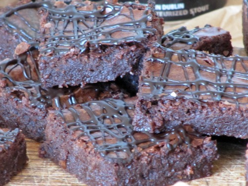 close-up of a pile of fudgy chocolate Guinness Stout brownies drizzled with chocolate on a wooden cutting board.