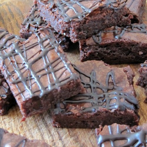 Several chocolate guiness fudge brownies drizzled with chocolate sitting on a wood cutting board