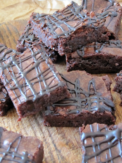 Several chocolate guinness Stout brownies drizzled with chocolate sitting on a wood cutting board.