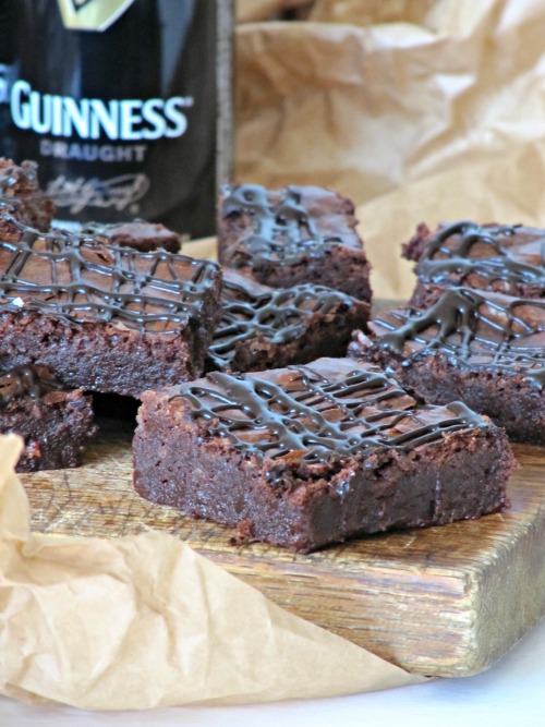 Several rich fudgy chocolate Guinness stout brownies on a wood chopping block in front of a bottle of Guinness Stout.